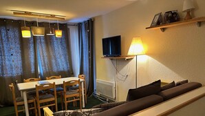 Ein gemütlicher Wohnbereich mit einer Couch, einem Esstisch mit Stühlen, einem an der Wand befestigten Fernseher und einer Lampe.