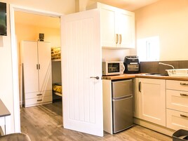 Cocina pequeña con armarios blancos, microondas, tostadora y refrigerador.