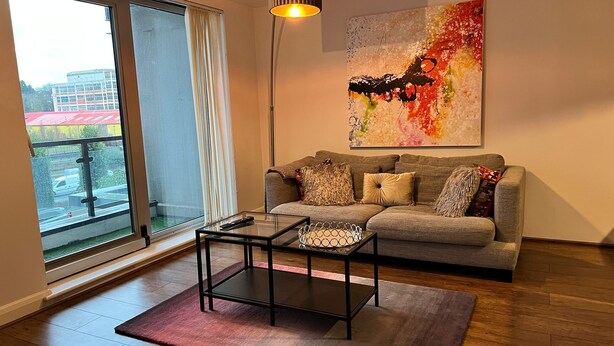 Una sala de estar moderna con un sofá gris, una mesa de centro de vidrio y un cuadro abstracto grande en la pared.