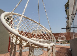 A macrame hanging chair in an outdoor area with a building in the background.