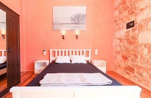 A bedroom with a wooden bed, white nightstands, a stone wall, and a painting of a landscape.