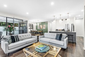 A modern living room with two sofas, a coffee table, and a dining area with a kitchen in the background.