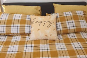 En säng med ett rutigt överkast och två kuddar, varav den ena har ordet ”happy” på sig.