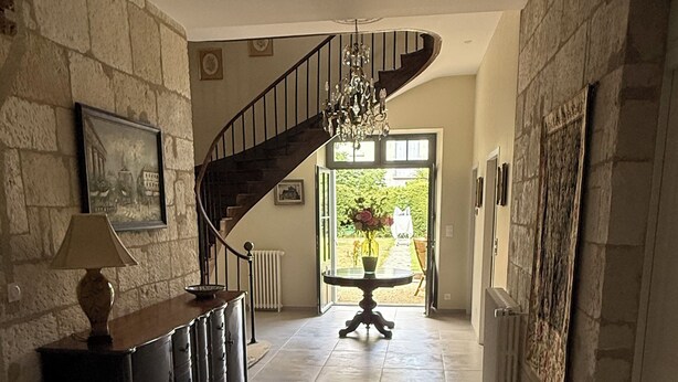 Ein Flur mit Treppe, einem Chandelier, einem Tisch mit Blumen und Blick ins Freie.