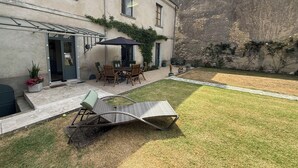 Eine Terrasse mit Tisch und Stühlen, ein überdachter Sitzbereich und eine Rasenfläche.