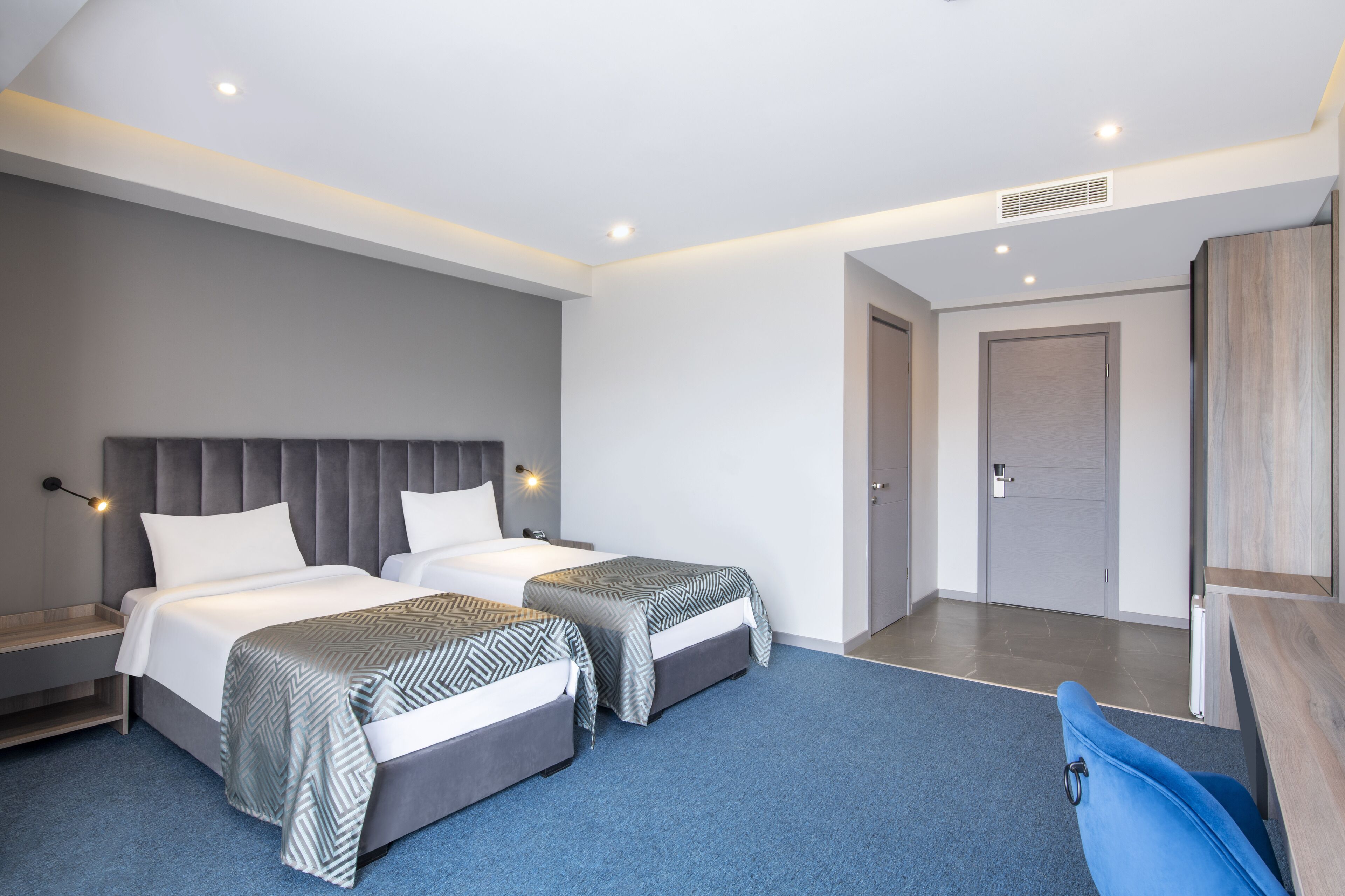 Une chambre d’hôtel moderne avec deux lits, une moquette bleue et un bureau en bois.