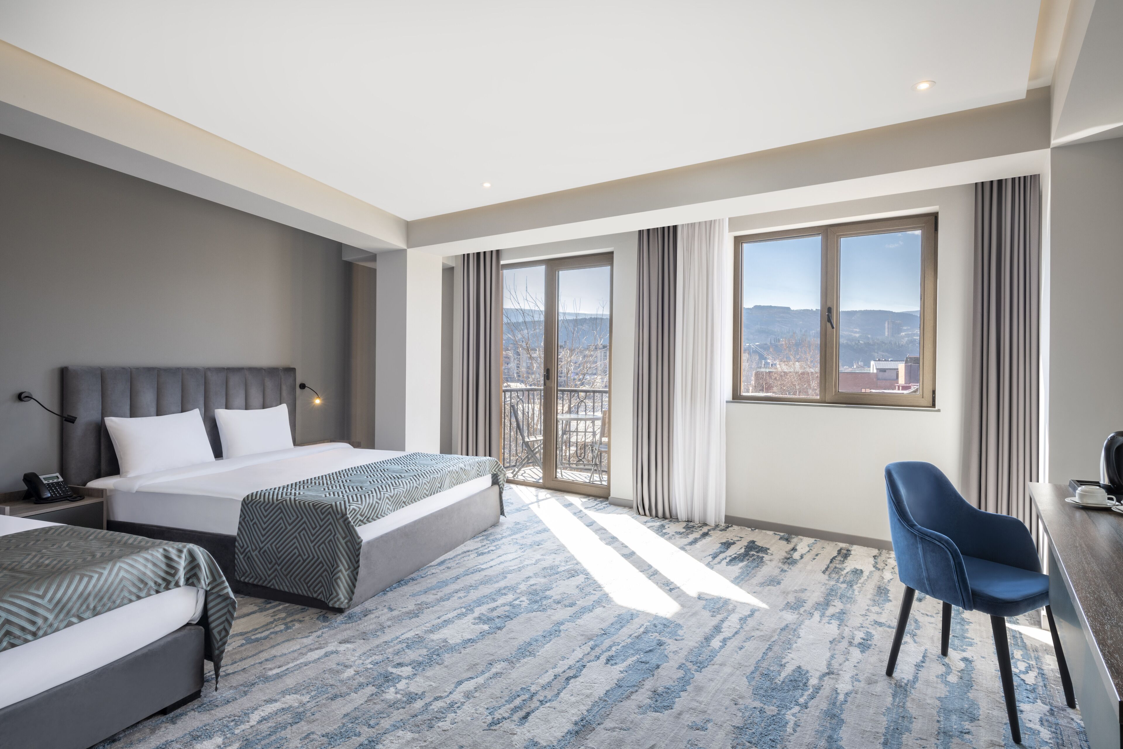 A modern hotel room with a large bed, a desk, and a view of the city.
