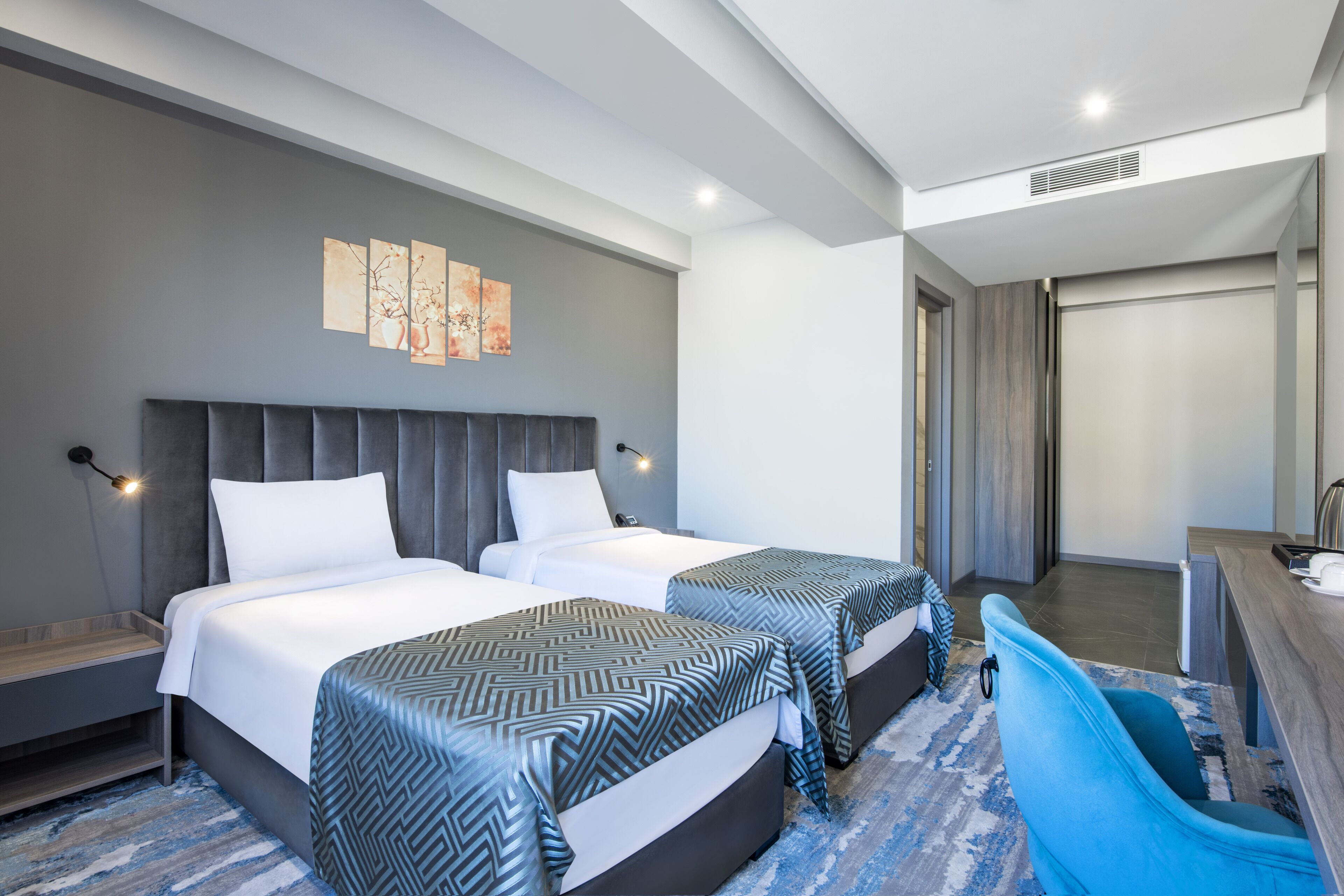 A hotel room with two beds, a desk, a chair, and a bathroom.