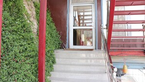 Eine Treppe aus Stein führt zu einer Tür mit Fensterglas, umgeben von roten Geländern und Grünpflanzen.