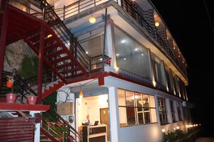 Un edificio de varios pisos con una escalera roja, ventanas grandes e iluminación exterior.