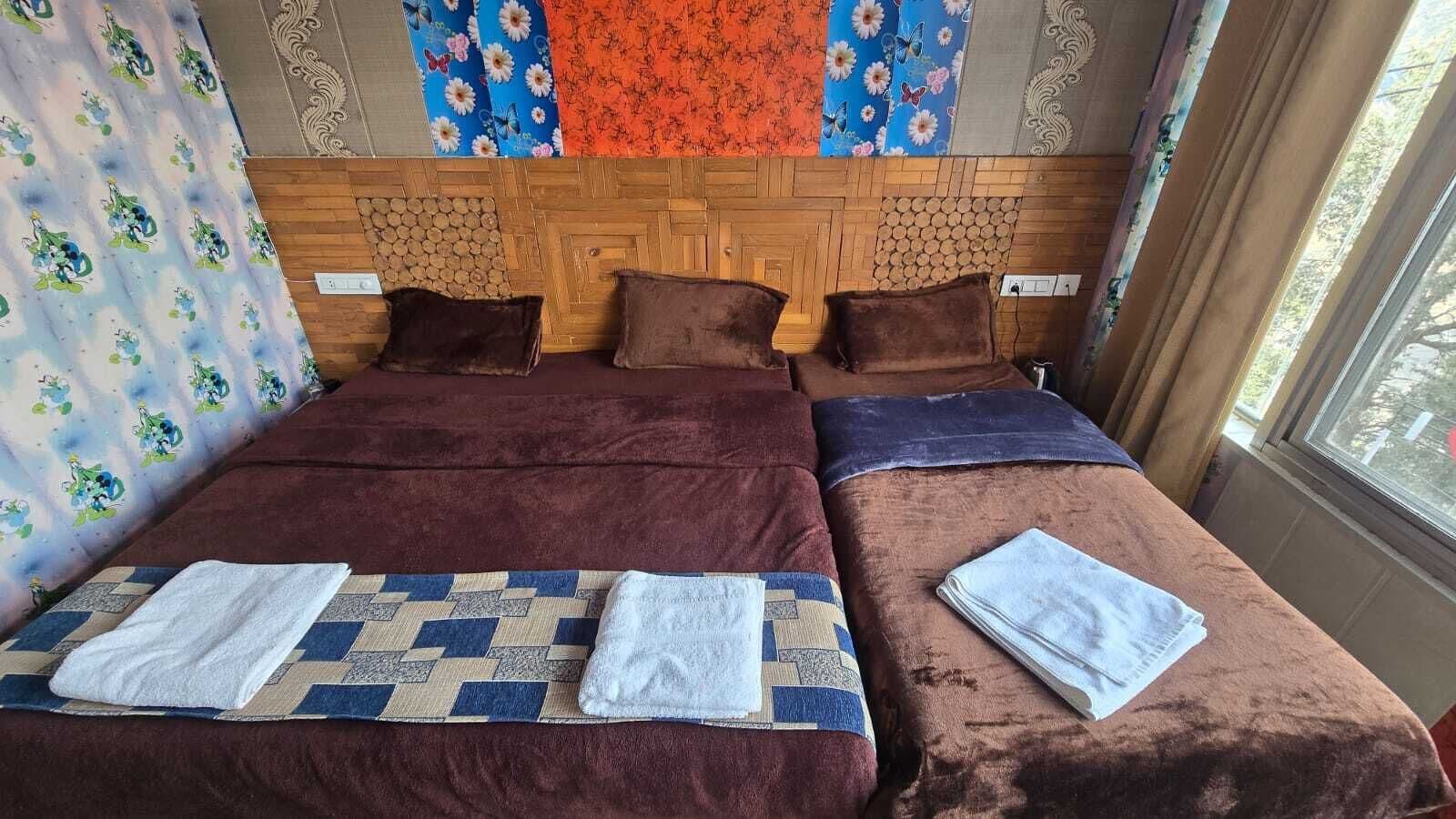 Una cama doble con cabecera marrón y dos almohadas, un edredón estampado en azul y beige, y una toalla blanca a cada lado.