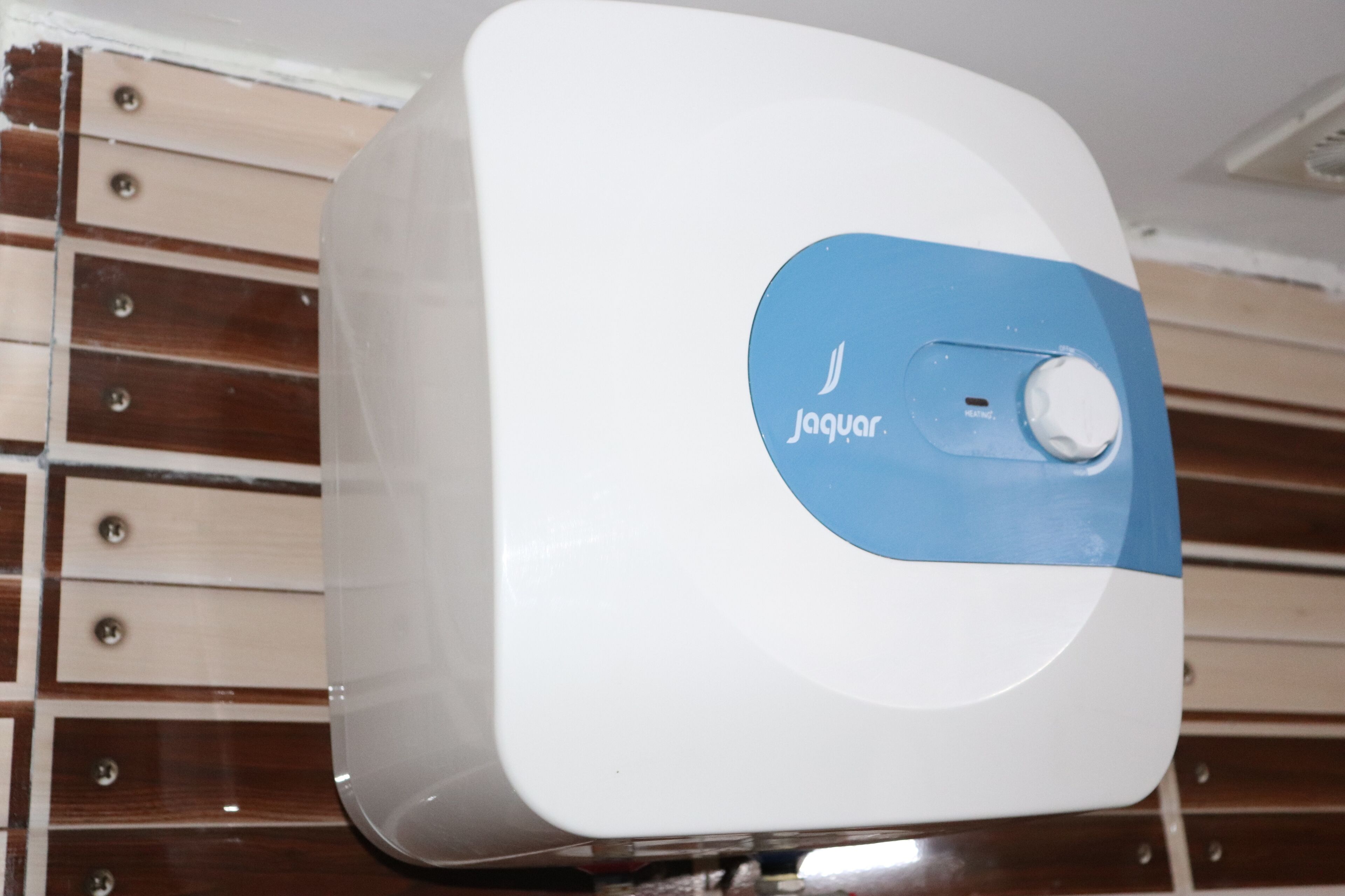 A white and blue device with a Jaguar logo and a button, placed on a wooden surface with drawers.