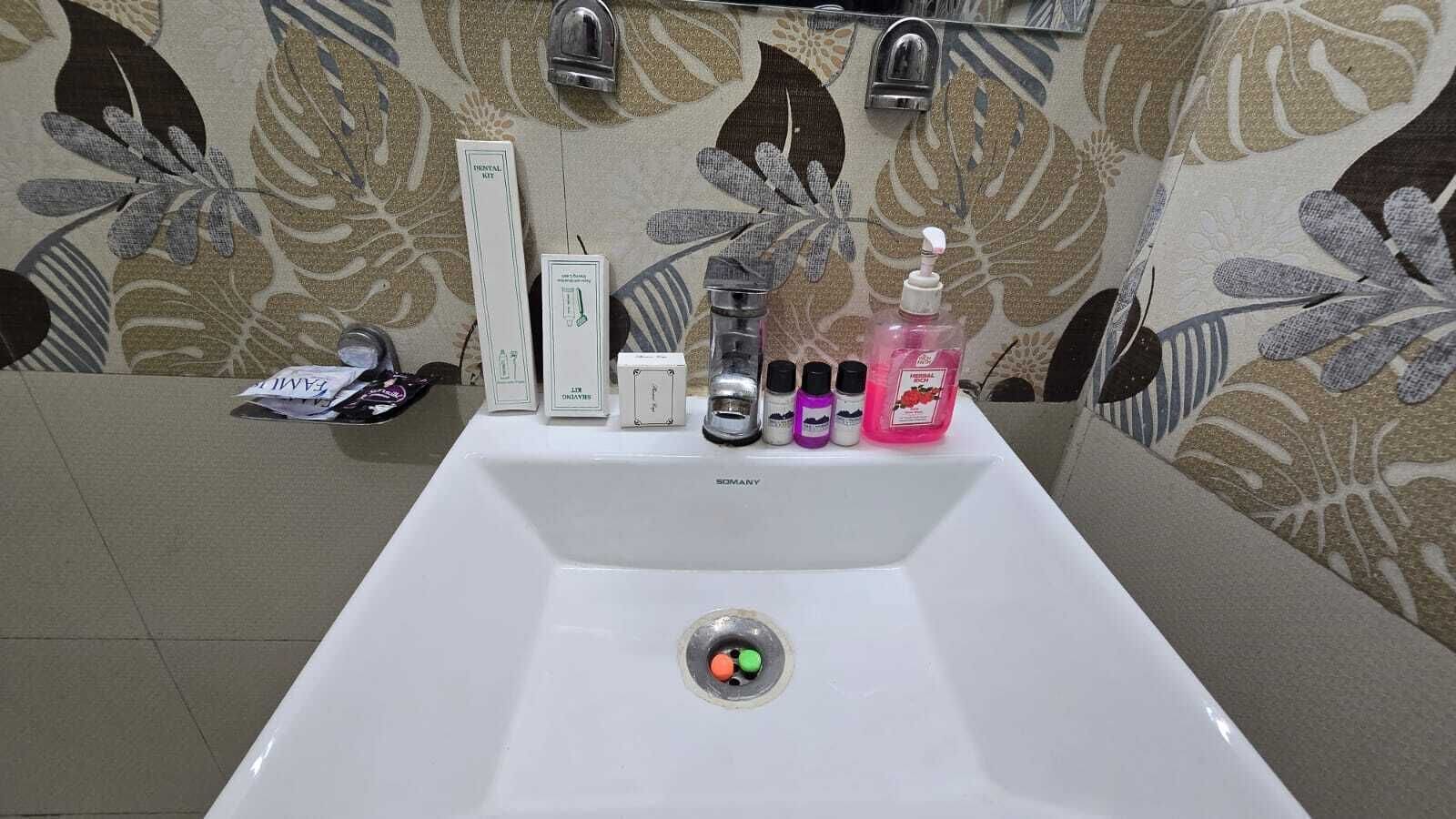 Een badkamermeubel met een bloemenpatroon op de muur, een spiegel en toiletartikelen zoals een zeepdispenser, shampoo en een tandenborstel.