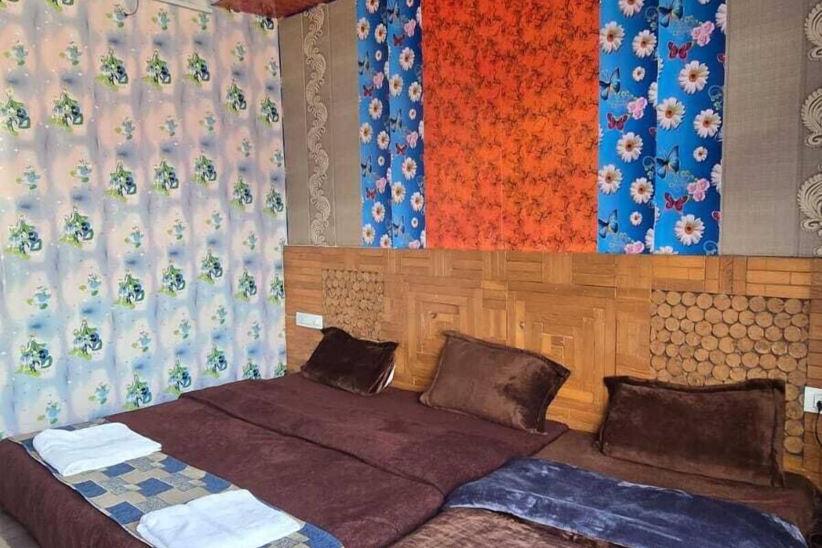 Une chambre à coucher avec une tête de lit en bois, deux lits avec une literie marron et bleue, un ventilateur de plafond et un papier peint à motifs floraux.