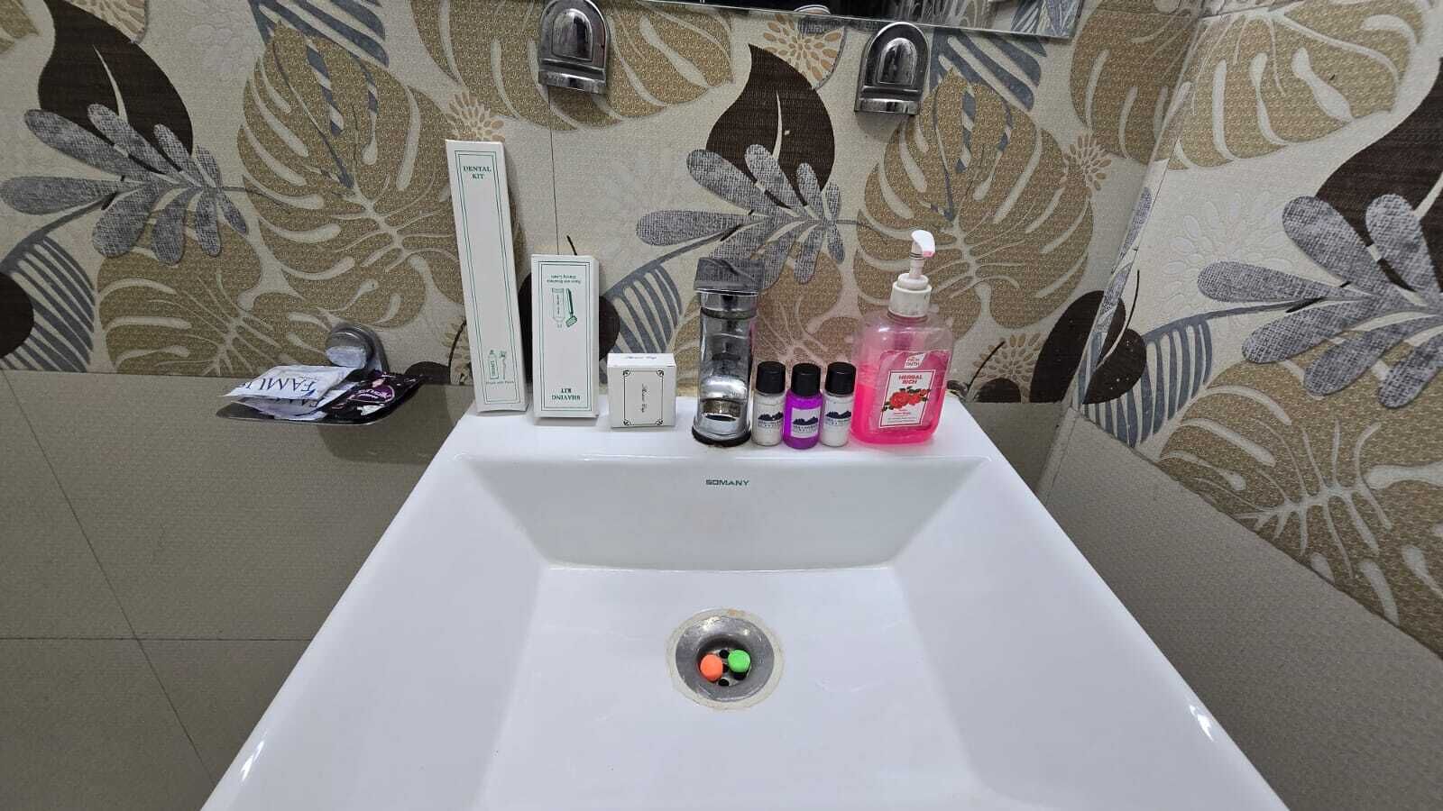 A bathroom sink with a floral-patterned wall, a mirror, and various toiletries.
