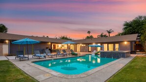 A backyard with a swimming pool, lounge chairs, umbrellas, and a house with a patio. - 2 Modern Villas On the Golf Course | Putting Green, Pool, Hot Tub | Sleeps 22 (La Quinta)