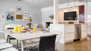 A modern kitchen with a dishwasher, a dining area with a table and chairs, and a living room with a sofa and artwork on the walls. - 2 Modern Villas On the Golf Course | Putting Green, Pool, Hot Tub | Sleeps 22 (La Quinta)