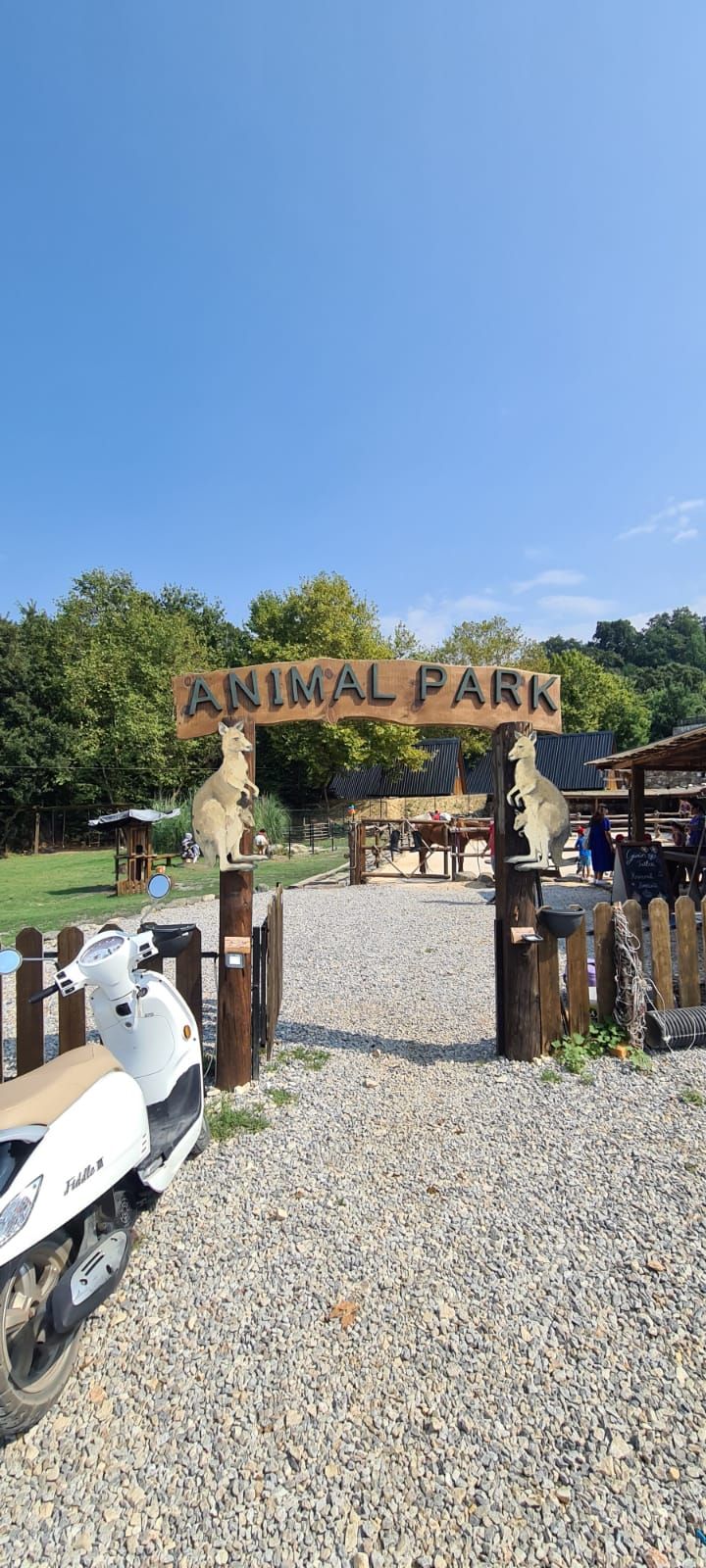 A sign for an animal park with a wooden gate and a scooter parked in front.