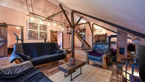 Un loft amplio con vigas de madera a la vista, una chimenea y una zona de estar acogedora con sofás de cuero y una mesa de centro.