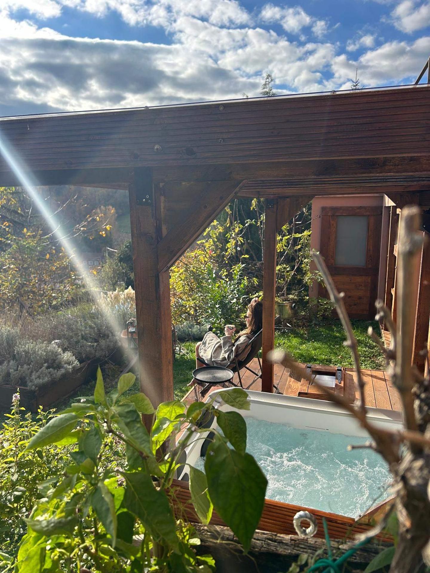 Una terraza de madera con un jacuzzi, rodeada de follaje y un cielo despejado.