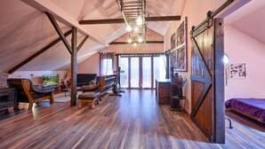 A spacious loft bedroom with a sloped ceiling, wooden beams, a large window, a bed, a dresser, and a hanging light fixture. - Villa Chill House Keti - Private Pool and Jaccuzzi (Mihovljan)