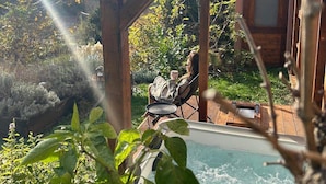 Una terraza de madera con un jacuzzi, rodeada de abundante vegetación y un cielo despejado.