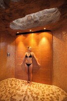 En kvinde i en sort bikini står i et flisebelagt rum med et unikt loftdesign og et mosaikgulv.