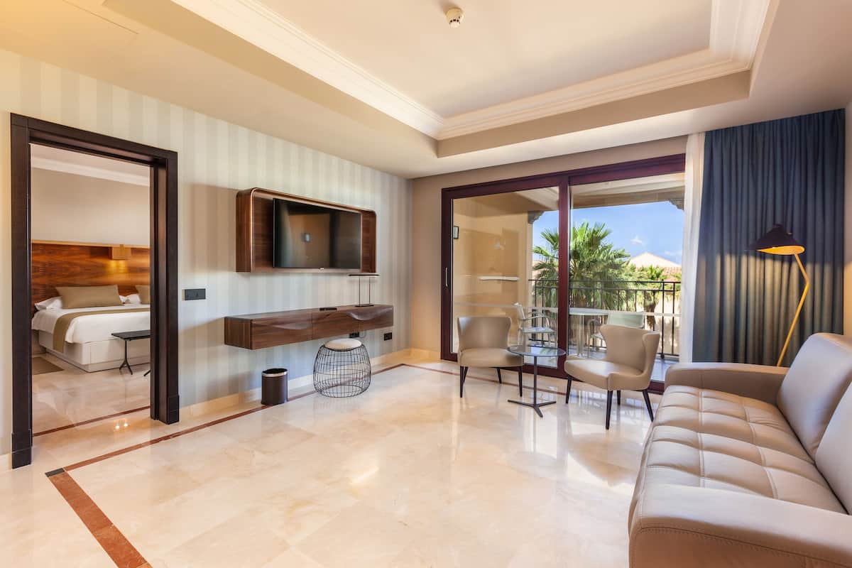 Une chambre d’hôtel moderne équipée d’un lit, d’une télévision, d’un balcon avec des chaises et d’un canapé.