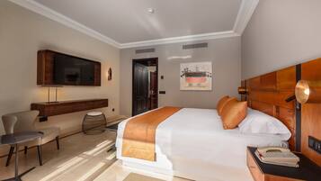 A hotel room with a large bed, a desk with a lamp, a television mounted on the wall, and a painting on the wall.