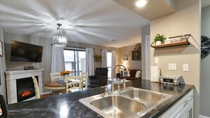 A modern kitchen with a black granite countertop, stainless steel sink, and a fireplace.