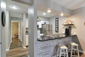 A modern kitchen with a marble countertop, two bar stools, a stainless steel refrigerator, and a 'MARKET' sign on the wall.