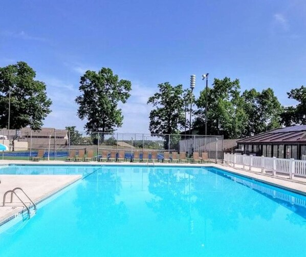 A clear blue swimming pool with a fenced area, surrounded by trees and a covered seating area.