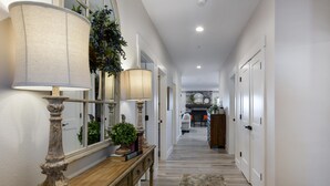 A hallway with a wooden console table, two lamps, a mirror, and a plant. There is a rug on the floor and a door at the end of the hallway. - Journey's Remedy Lite - Lake View - Closest to Indoor Pool - Sleeps 22 (Branson)