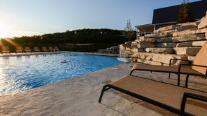A swimming pool with lounge chairs, a stone wall, and a view of trees in the background. - Journey's Remedy Lite - Lake View - Closest to Indoor Pool - Sleeps 22 (Branson)