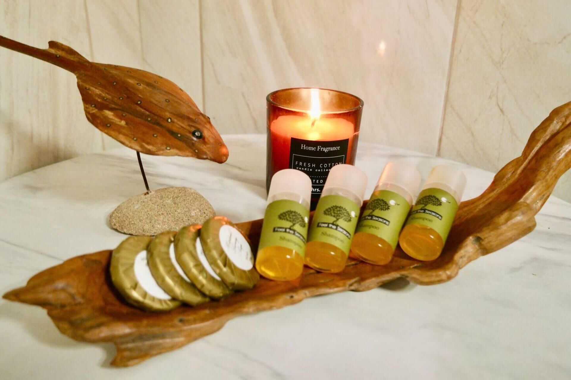 A wooden leaf-shaped tray with a candle, a rock, and three small bottles.