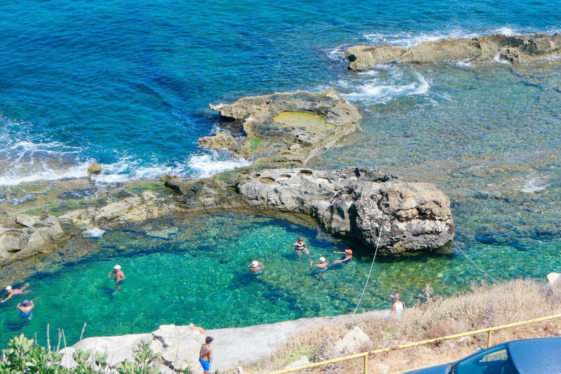 A coastal area with clear water, rocky formations, and people swimming.