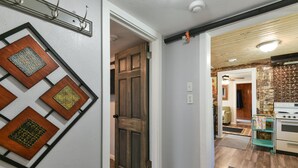 Un couloir avec une porte en bois, un coin cuisine avec un fourneau et un mur orné de cadres carrés décoratifs.