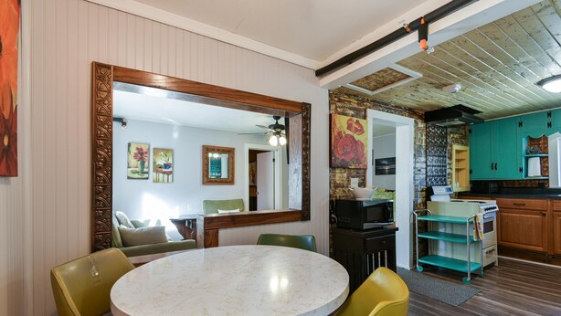 Un coin repas avec une table ronde et des chaises, une cuisine avec des meubles en bois et un grand miroir au mur.
