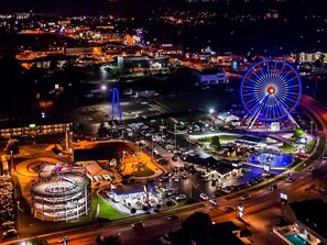 An aerial view of a cityscape at night with a prominent Ferris wheel, a roundabout, and a parking area.