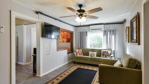 Un salon avec un canapé, un tapis, un ventilateur de plafond et un téléviseur fixé au mur.