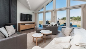 Una sala de estar moderna con chimenea, ventanas amplias y vista a la playa.