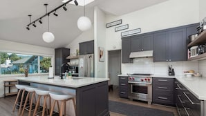 Una cocina moderna con armarios oscuros, una isla grande con taburetes, horno empotrado y vistas al exterior.