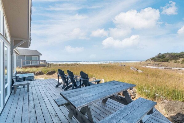A wooden deck with a table and chairs, overlooking a beach and dunes.