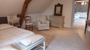 A bedroom with a sloped ceiling, a bed with a floral bedspread, a chair, a dresser, and a mirror. - La chouett'chambre" bed and breakfast (Les Hermites)