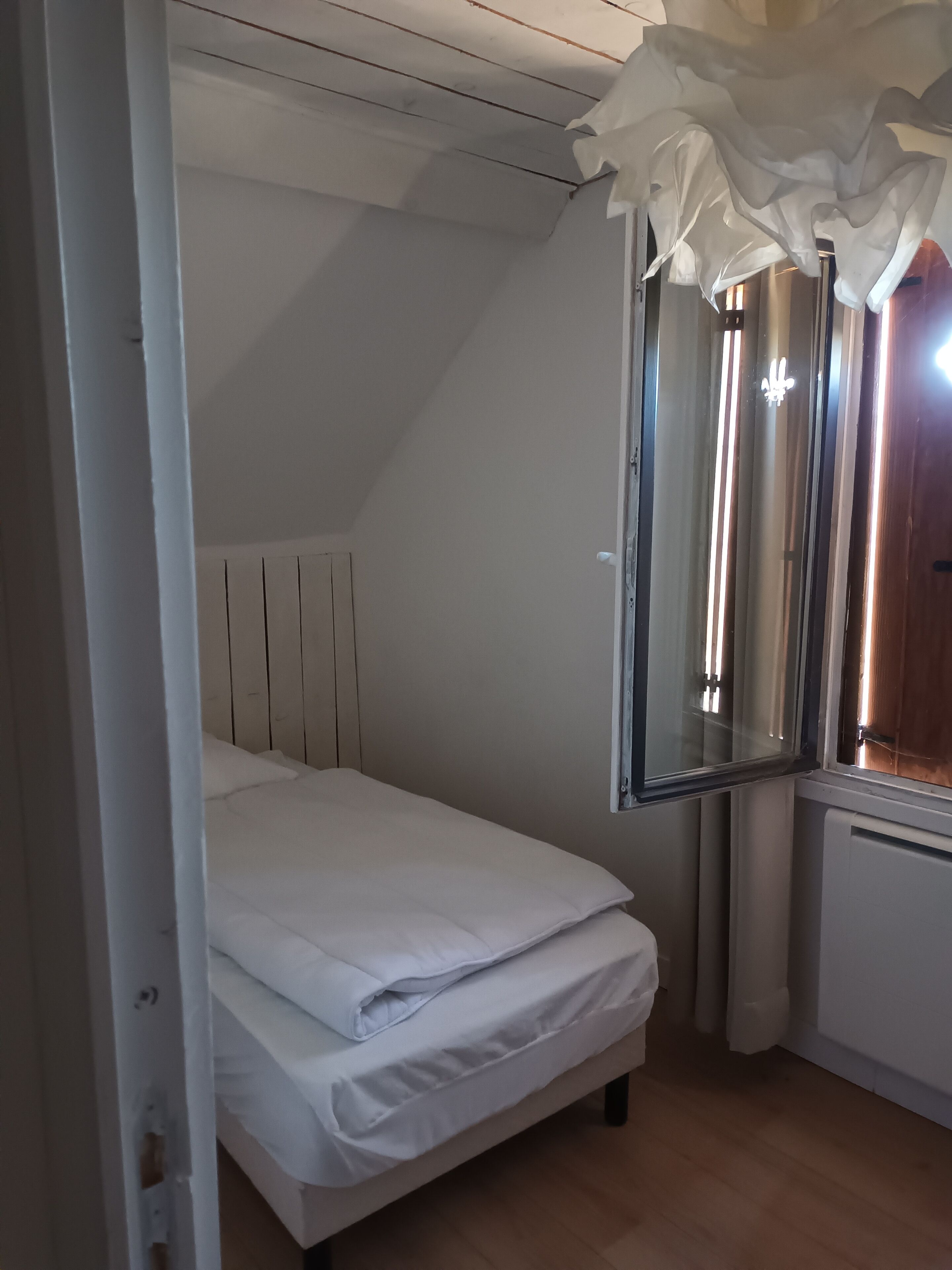 Ein Schlafzimmer mit einem Einzelbett, einem Fenster mit Vorhängen und einer Heizung.