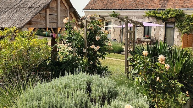 A rustic garden with wooden structures, a weather vane, and a stone building with a tiled roof. - La chouett'chambre" bed and breakfast (Les Hermites)