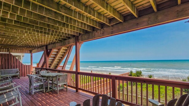 A wooden deck with Adirondack chairs and a table, overlooking the ocean. - Sunny Turtle: Turtle-tastic Oceanfront Stay! (Surf City)
