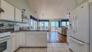 A spacious kitchen with white cabinets, a central island, and a large refrigerator. - Sunny Turtle: Turtle-tastic Oceanfront Stay! (Surf City)