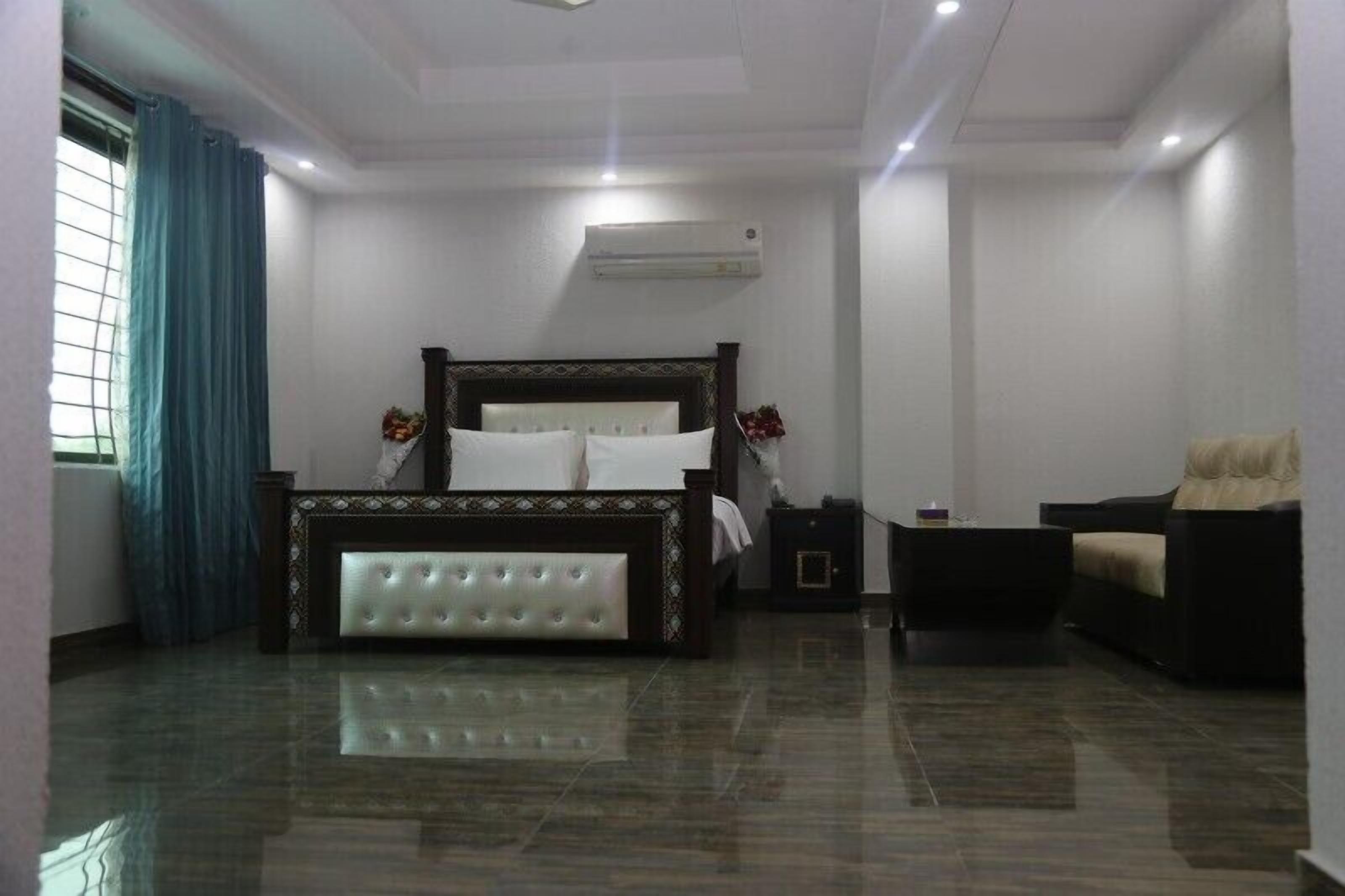 A bedroom with a large bed, a nightstand, a chair, and an air conditioning unit.