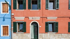 A building with multiple windows, some with shutters, and a central door with a decorative pattern. - Wondrous Palazzetto 1619 in Magical Burano Island (Burano)